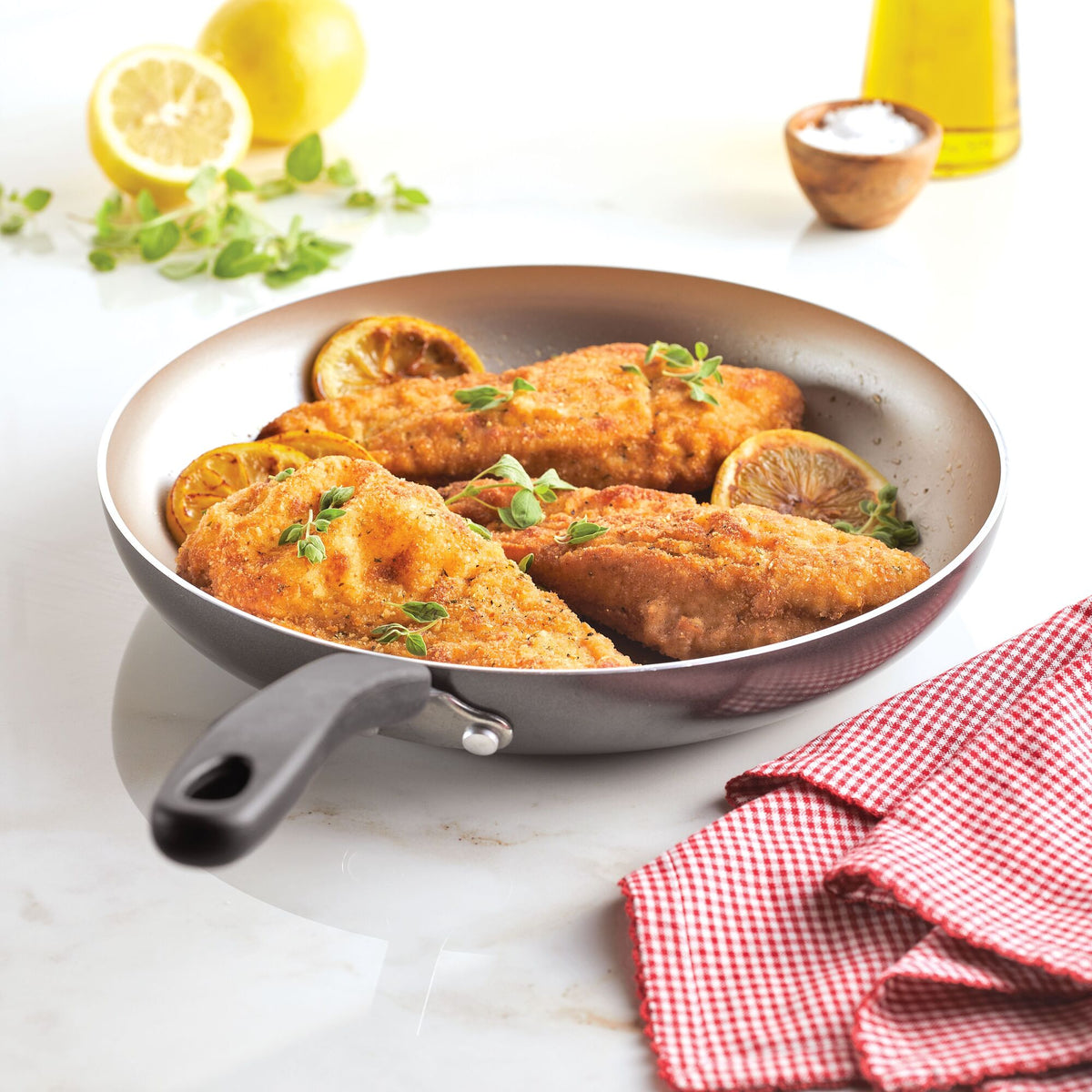 Fried fish fillets with lemon slices in a pan, resting on a countertop.