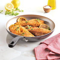 Fried fish fillets with lemon slices in a pan, resting on a countertop.