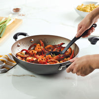 Person stirring shrimp dish in a frying pan on a kitchen countertop.