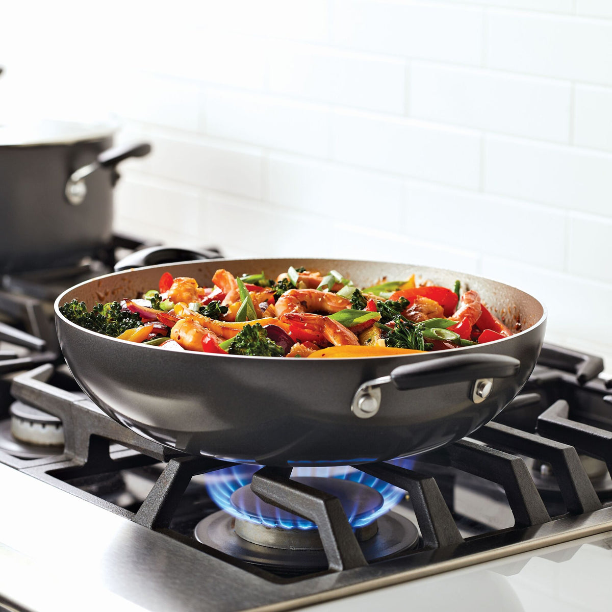 Stir-fry vegetables cooking in a black pan on a gas stove.
