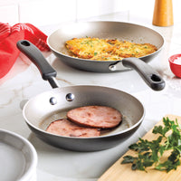 Two frying pans with ham and hash browns on a kitchen countertop.