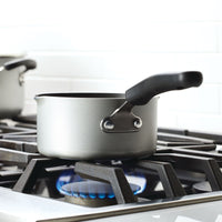 A saucepan on a lit gas stove burner in a kitchen setting.