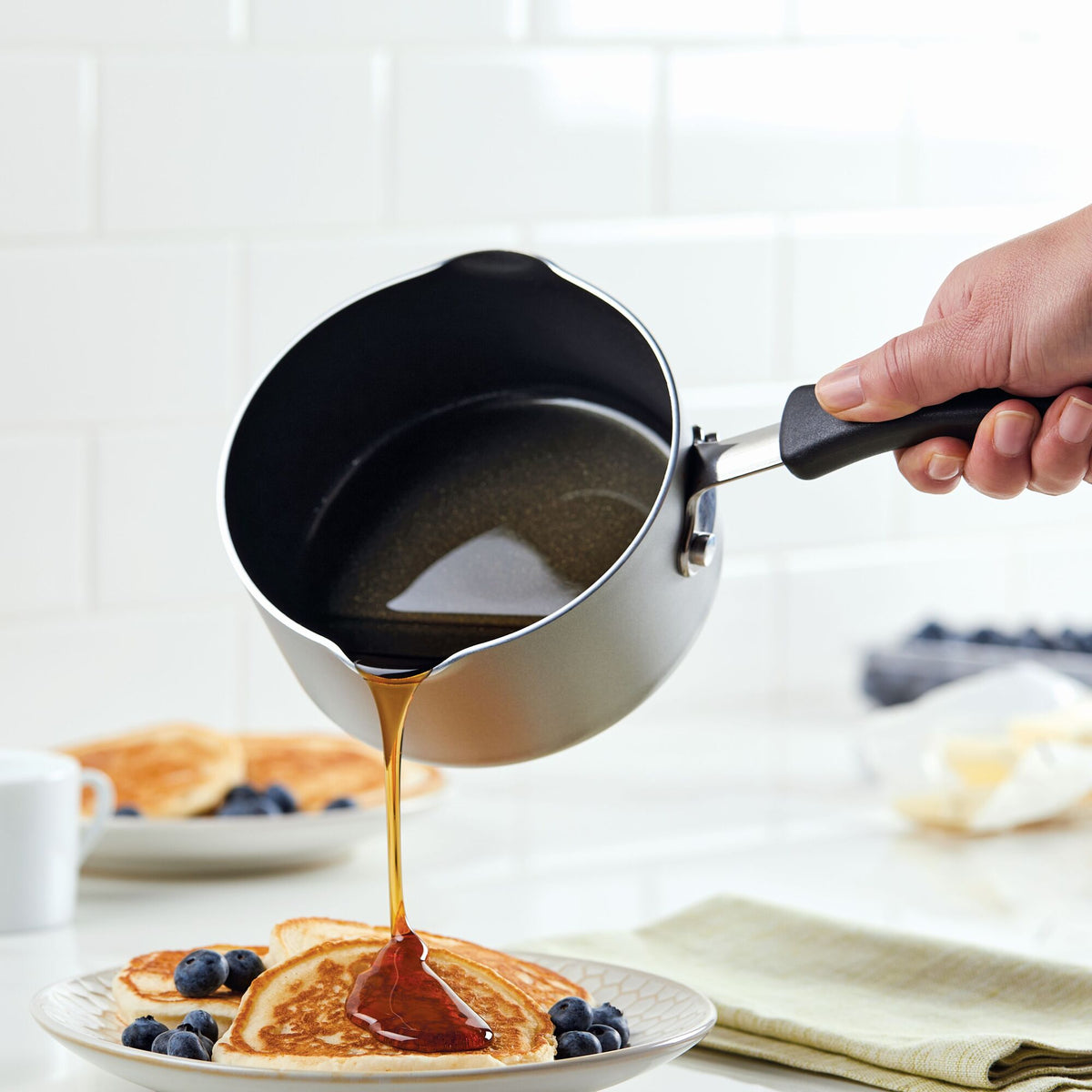 Pouring syrup onto pancakes on a plate with blueberries.