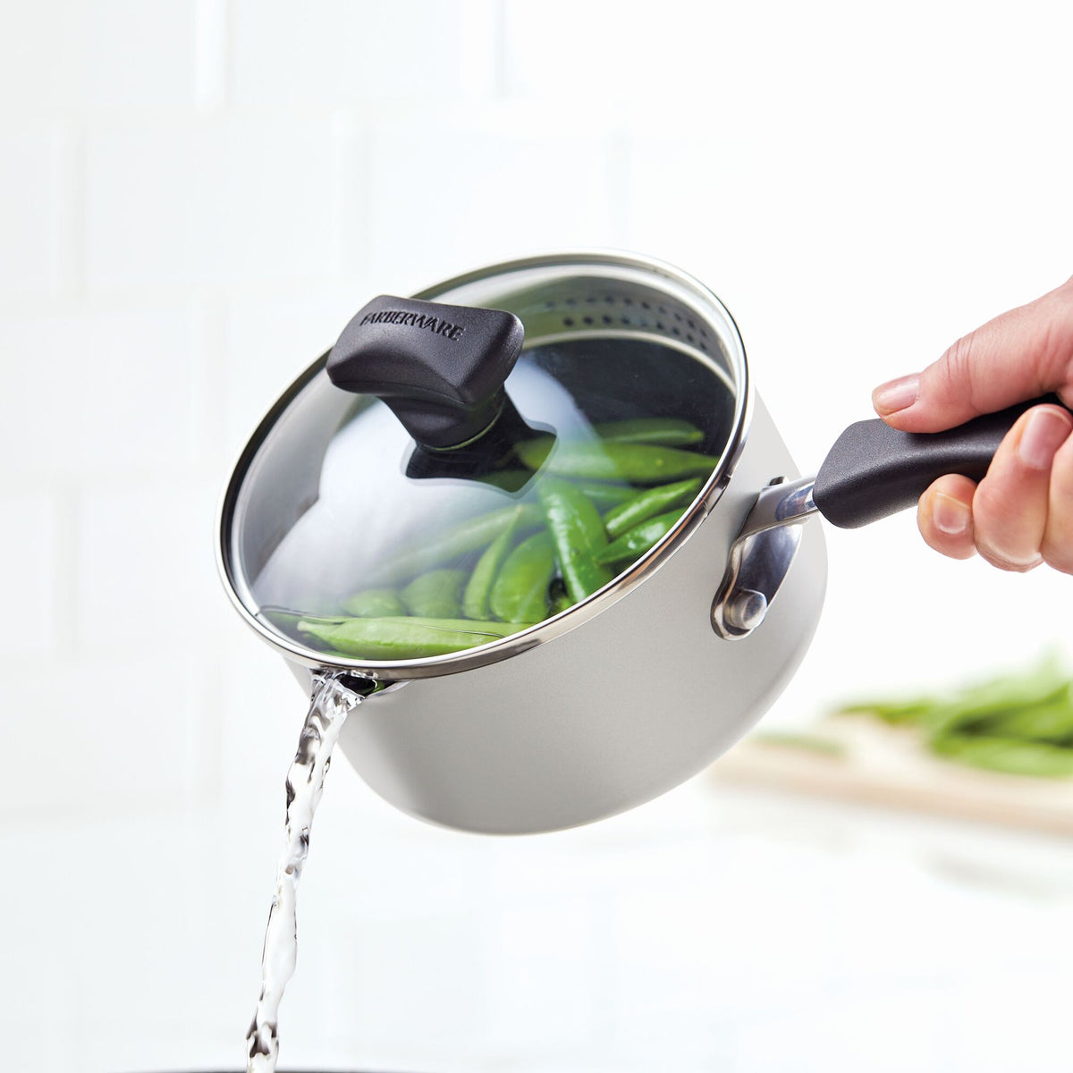 Pouring water from a pot of green beans using a strainer lid.