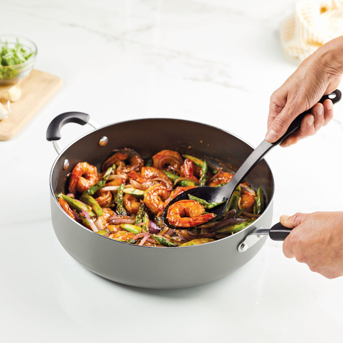Hands stirring a vegetable and shrimp stir-fry in a pan.
