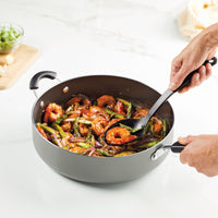 Hands stirring a vegetable and shrimp stir-fry in a pan.