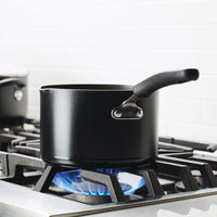 A black saucepan on a stove with blue flames beneath it.