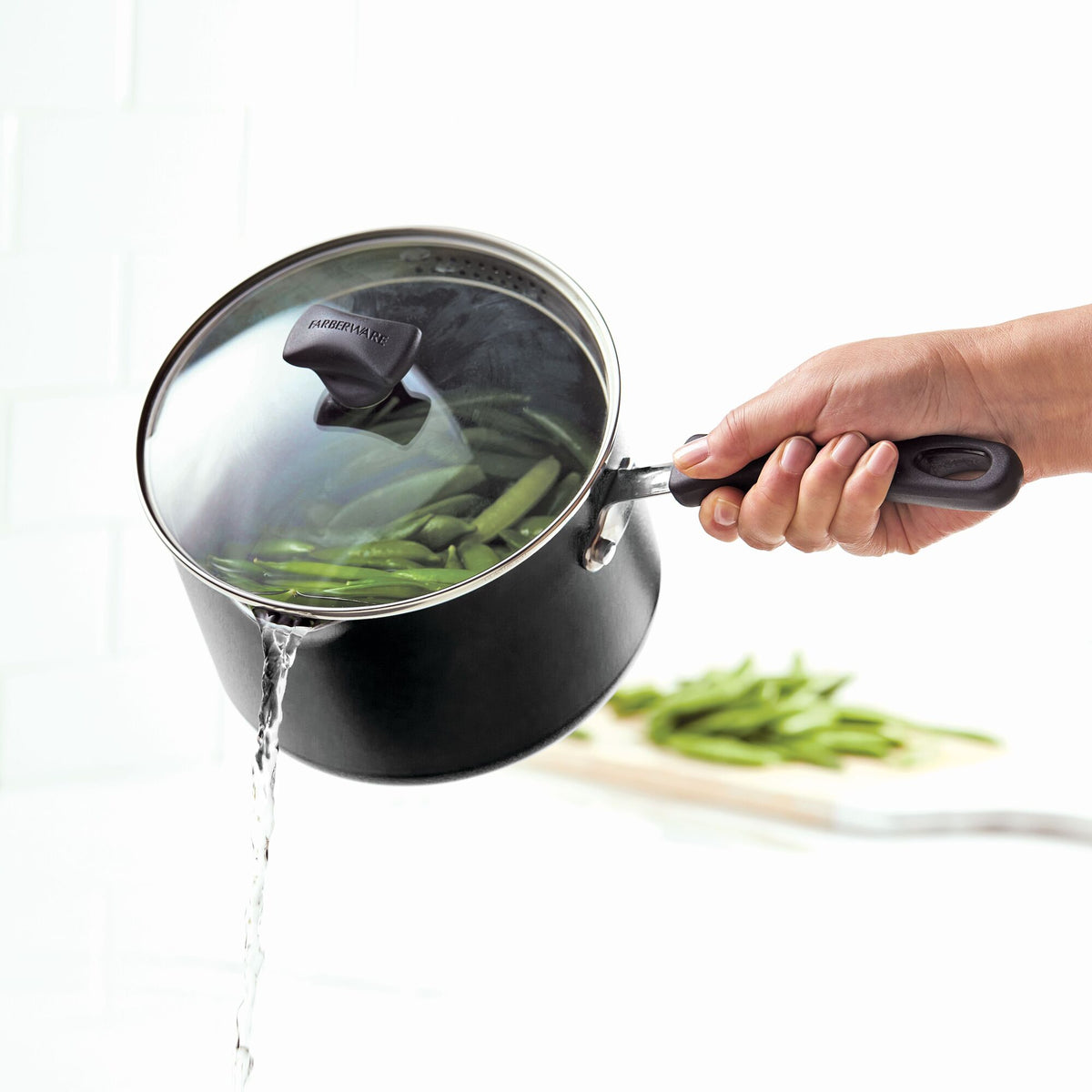 Straining green beans over the sink using a pot with a lid.