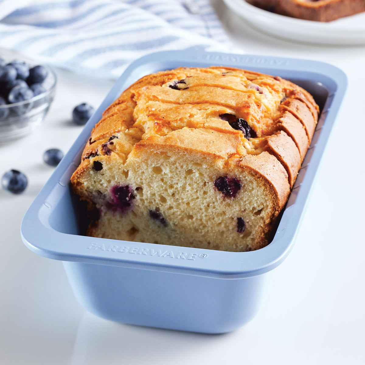 Sliced blueberry bread in a blue baking pan with fresh blueberries nearby.
