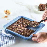 Person slicing brownies in a blue baking pan with a spatula.
