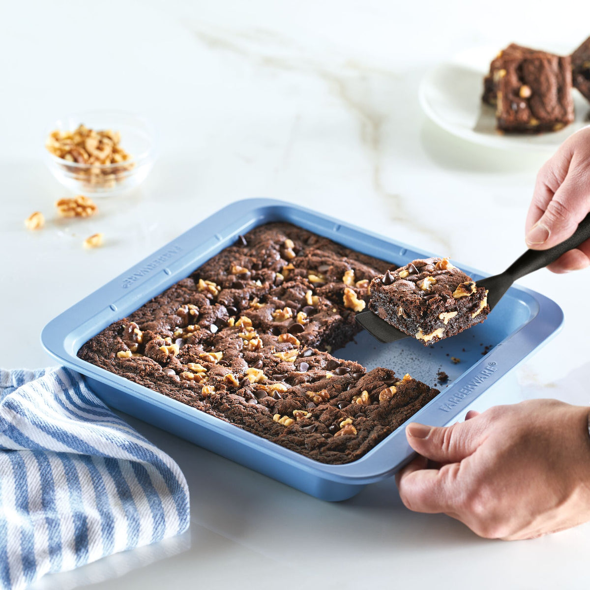 Person slicing brownies in a blue baking pan with a spatula.