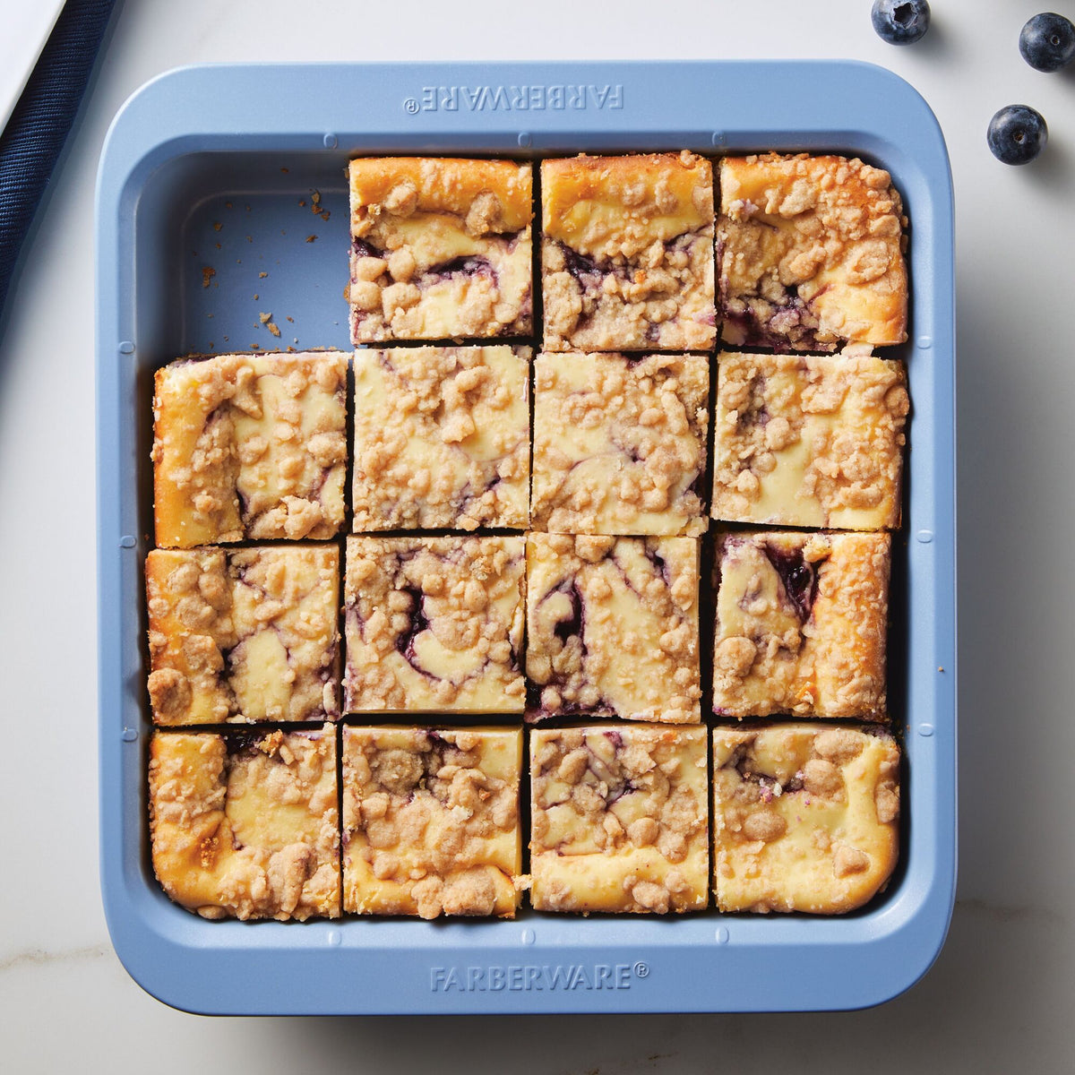 Blueberry crumble bars in a square baking dish on a white surface.