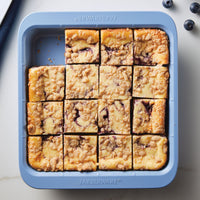 Blueberry crumble bars in a square baking dish on a white surface.