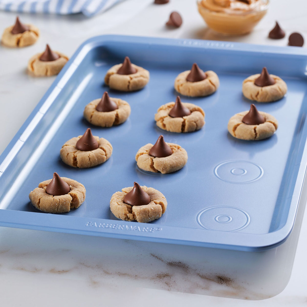 Baking tray with peanut butter blossom cookies topped with chocolate kisses.