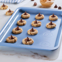 Baking tray with peanut butter blossom cookies topped with chocolate kisses.