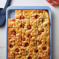 Baking tray of focaccia topped with cherry tomatoes and herbs.