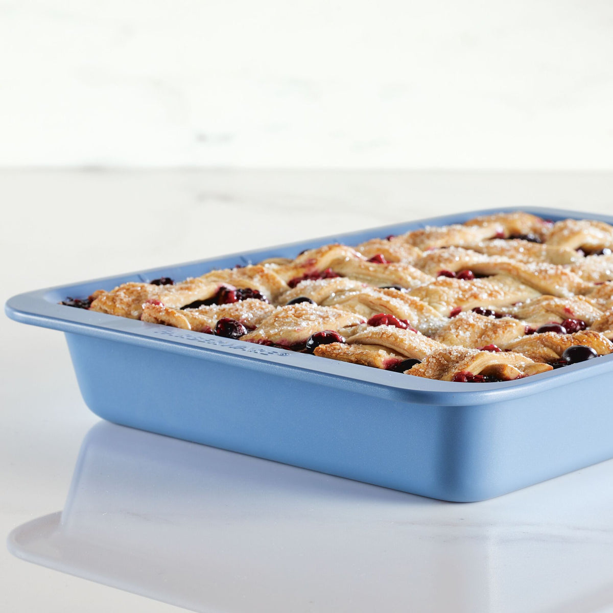 Pie with lattice crust in a blue baking dish on a white countertop.