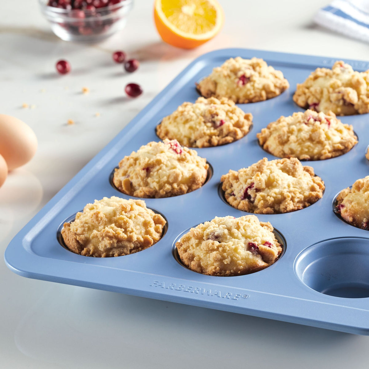 Muffins in a blue tray on a kitchen counter with ingredients around.