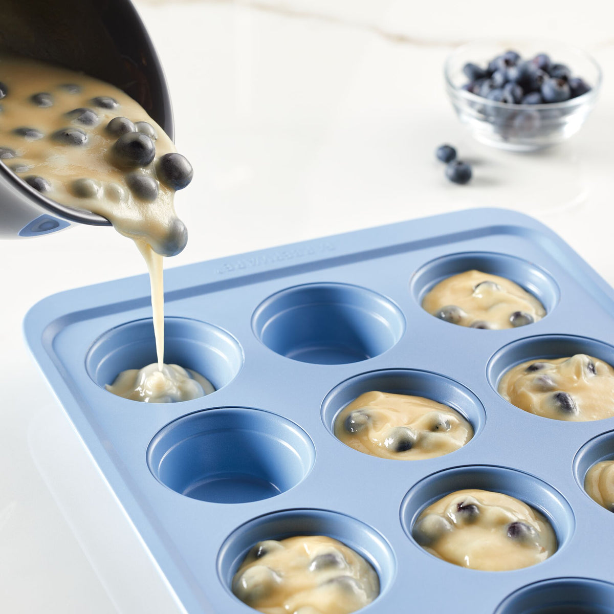 Pouring blueberry batter into a muffin tray.