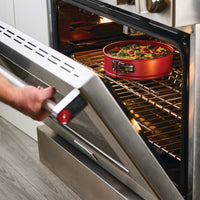 A person closes an oven with a dish inside on the rack.