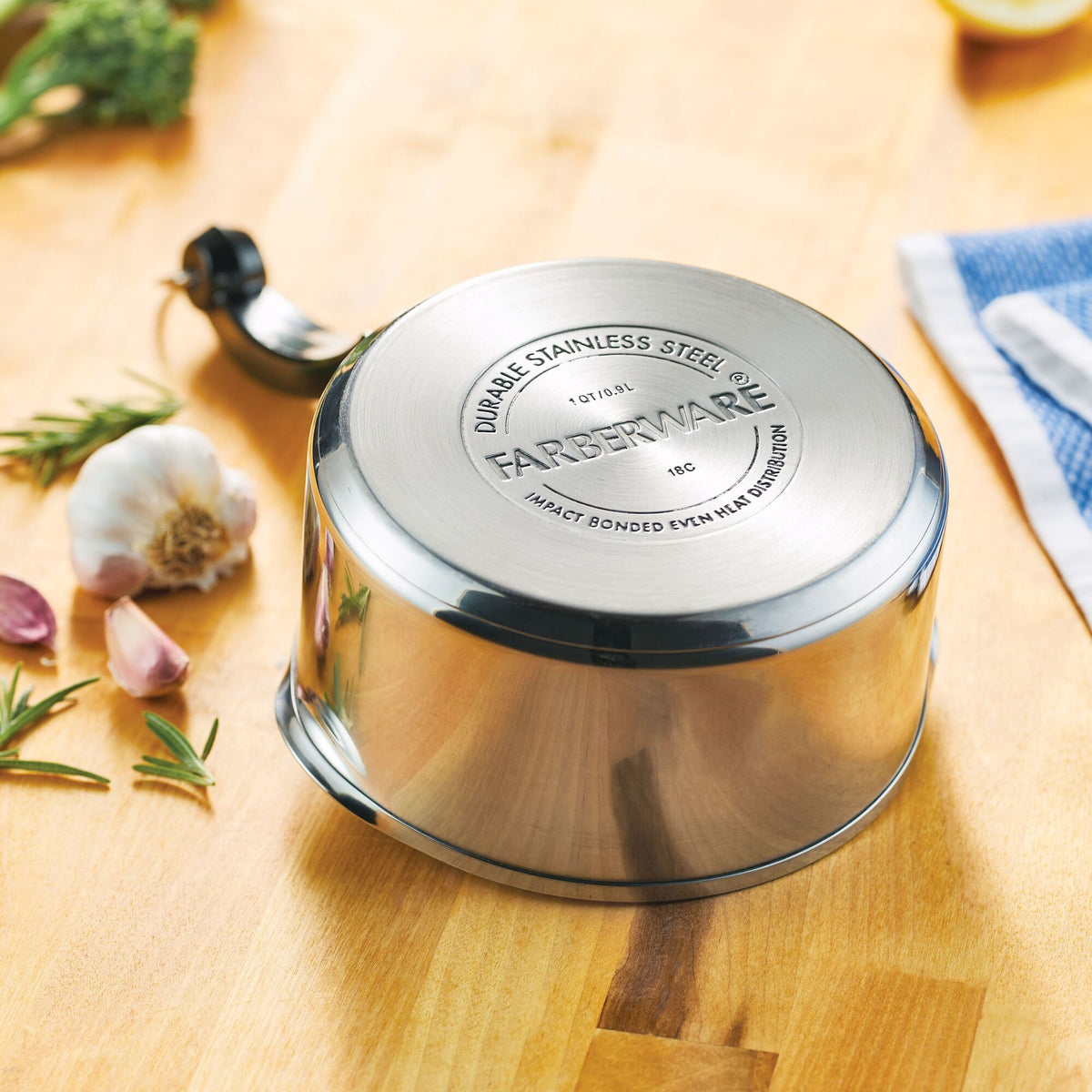 Stainless steel saucepan lid on wooden surface with garlic and herbs nearby.