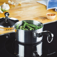 A pot of green beans on a stove next to a lid and spice bowl.