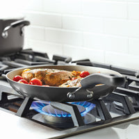 Chicken and tomatoes cooking in a skillet on a gas stove.