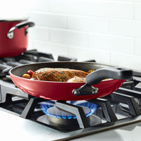 Red frying pan on a gas stove with chicken and vegetables cooking.