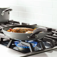 A frying pan with food cooking on a lit gas stove burner.