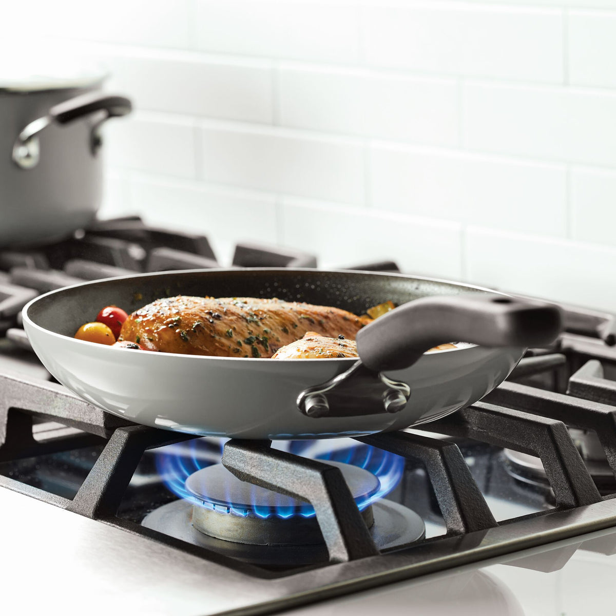 A frying pan with food cooking on a lit gas stove burner.