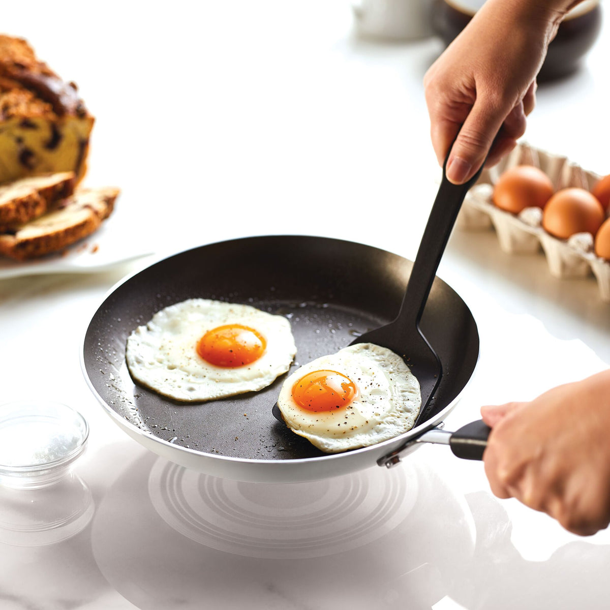 Person cooking two sunny-side-up eggs in a frying pan.
