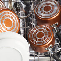 Copper pans and white plates arranged inside an open dishwasher.