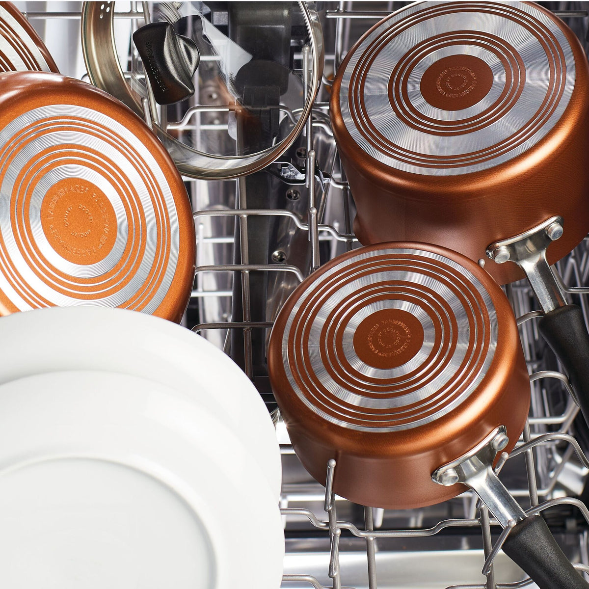 Copper pans and white plates arranged inside an open dishwasher.
