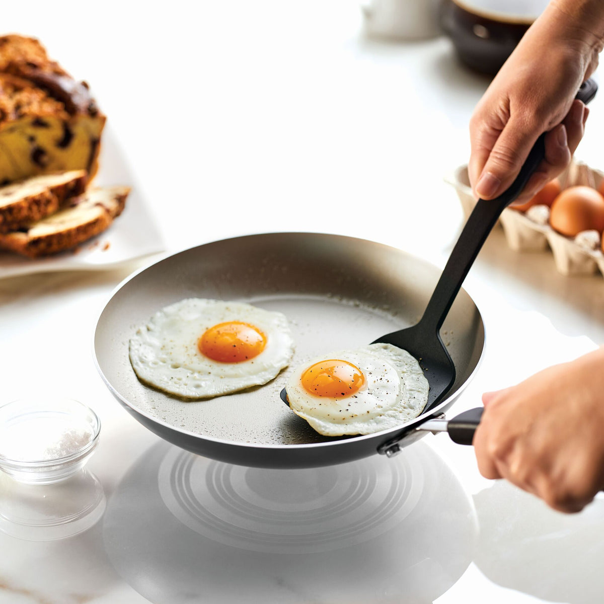 Person frying two eggs in a non-stick pan with a spatula.