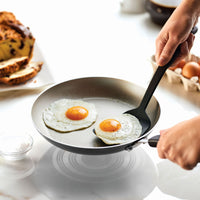 Person frying two eggs in a non-stick pan with a spatula.
