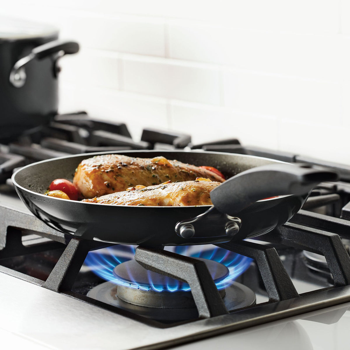 Chicken pieces are cooking in a black frying pan on a gas stove.