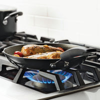 Chicken pieces are cooking in a black frying pan on a gas stove.