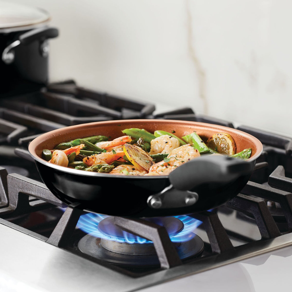 A frying pan on a stove with vegetables and chicken cooking over a flame.