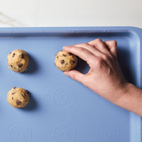 Hand placing cookie dough balls on a blue baking sheet.