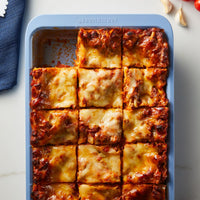 A pan of baked lasagna cut into square pieces.