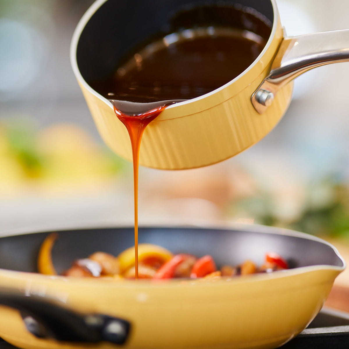 Pouring sauce from a yellow saucepan into a skillet with vegetables.