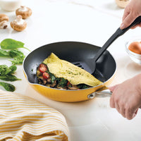 A person cooking a vegetable omelet in a yellow frying pan.