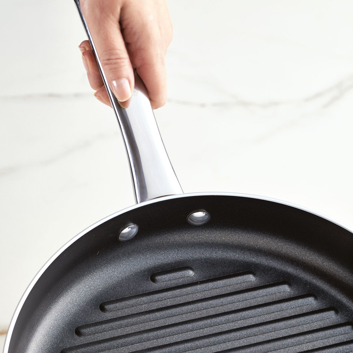 Hand holding a non-stick frying pan with a ridged cooking surface.