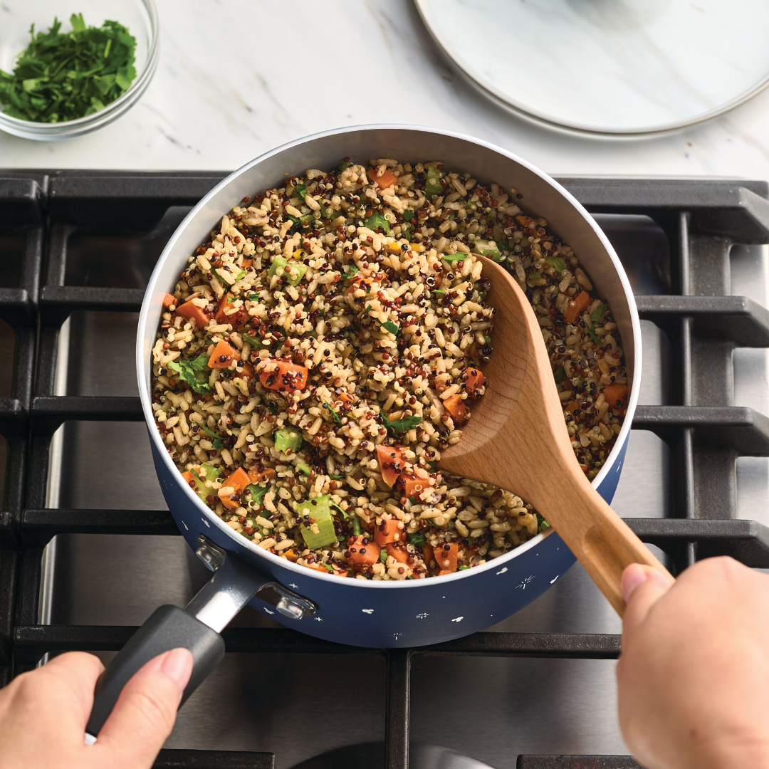 Person stirring cooked quinoa and vegetables in a pot on a stove.