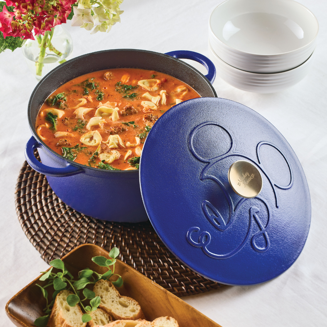 Blue pot with soup and tortellini, lid embossed with a pattern, on a table.