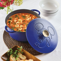 Blue pot with soup and tortellini, lid embossed with a pattern, on a table.