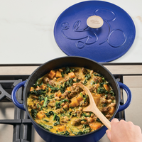 Pot of stew with vegetables and sausage on a stove, blue lid beside it.
