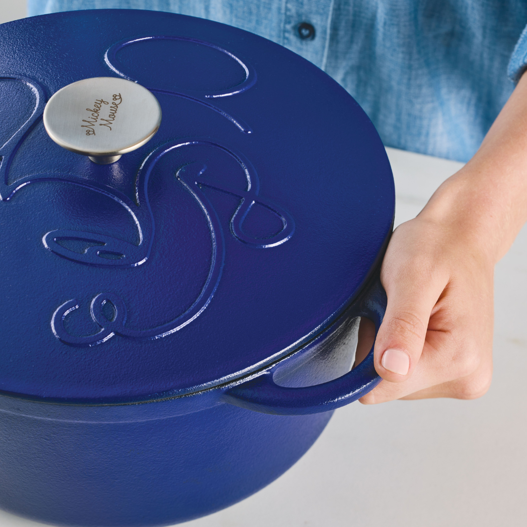 Hand holding the handle of a blue cast iron pot with a lid.