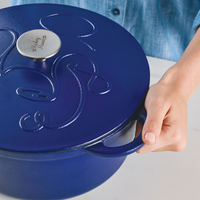 Hand holding the handle of a blue cast iron pot with a lid.