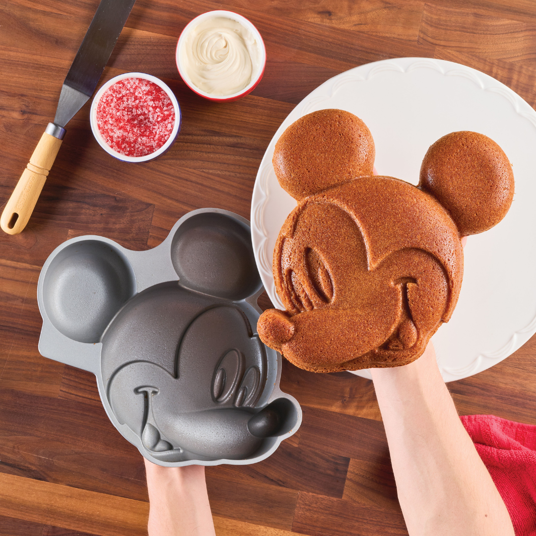 Hands holding a cake molded to resemble Mickey Mouse's iconic head, created with the Mickey Mouse 3D Cake Pan.